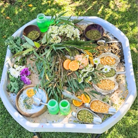 Tuff Tray ,in white, filled with sand, dried flowers, green leaves, orange slices, seeds, and small green bottles, photographed on grass.