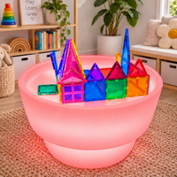 The round Sensory Light and Water Table lit in warm coral pink, casting colour across the rug