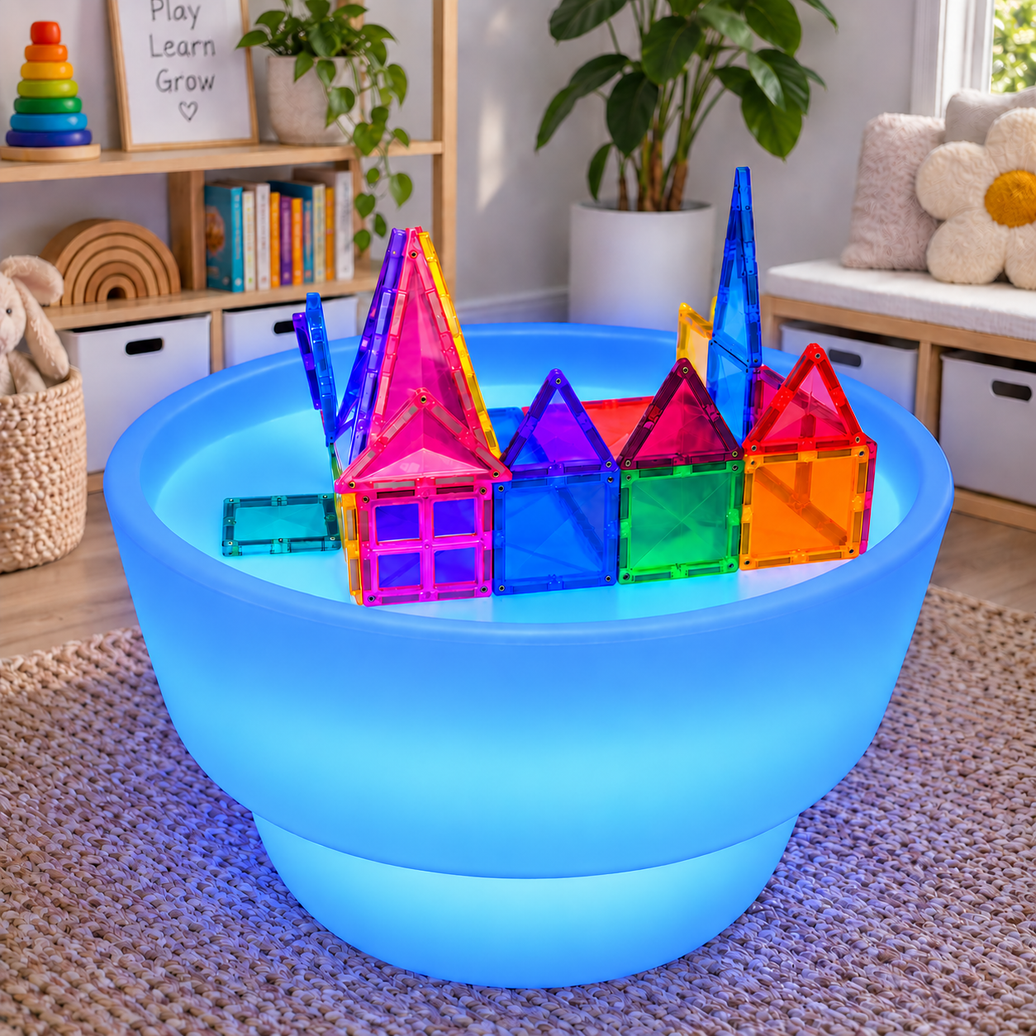 Sensory Light and Water Table glowing blue in a playroom, with a magnetic tile castle built on the surface