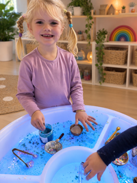 A smiling girl pouring water between the compartments of the Large Sensory Light and Water Table